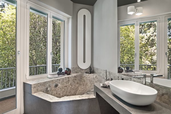 Interior view of a modern bathroom in the foreground the washbasin on the masonry top and in the corner on the background under the window there is the masonry bathtub