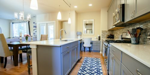 Modern home kitchen diner with green grey fitted units, a kitchen island and blue floor rug.