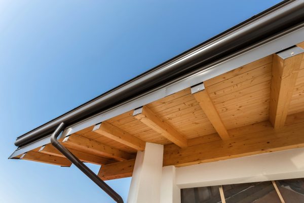 New wooden warm ecological house roof with steel gutter rain system. Professional construction and drainage pipes installation. Eco materials.