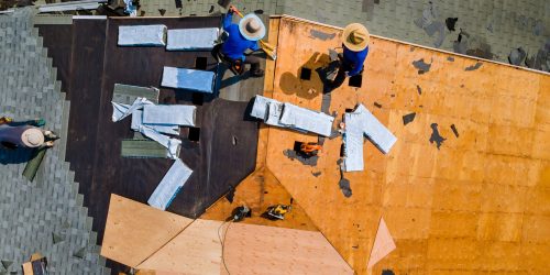 Aerial top view of construction roofer installing roof tiles at house building site at work installing roof shingles